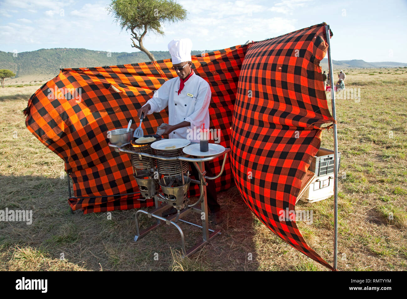 African chef cucinare la colazione sul palloncino bruciatori sulle pianure erbose dopo lo sbarco di palloncino, il Masai Mara, Kenya Foto Stock