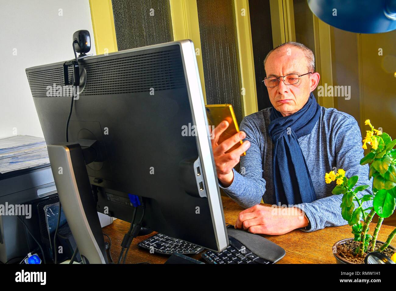 Uomo di mezza età con gli occhiali seduto alla scrivania. Uomo maturo utilizzando il telefono cellulare. Concetto senior. Man a home office Foto Stock