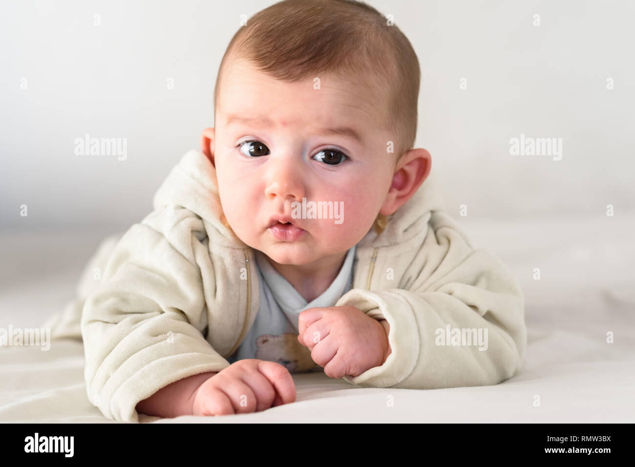 Bellissima e dolce neonato sdraiato a faccia in giù sul letto sollevando il capo a guardare la fotocamera curiosamente. Foto Stock