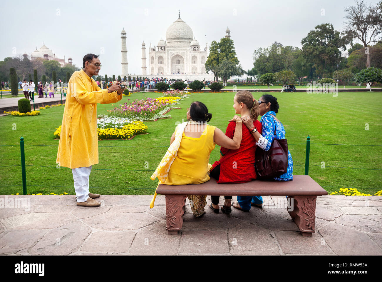 AGRA, Uttar Pradesh, India - Febbraio 24, 2015: famiglia indiana prendendo foto di gruppo con stranieri in abito rosso sul banco di lavoro nel giardino di fronte Taj Foto Stock