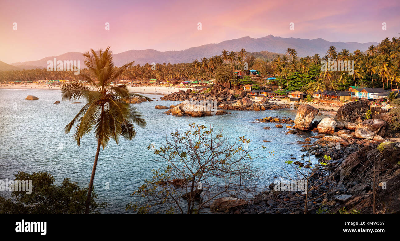 Bella vista panoramica del tramonto tropicale spiaggia con bungalow e palme di cocco a Palolem in Goa, India Foto Stock