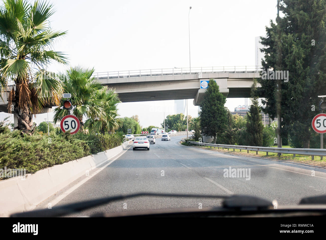 Izmir, Turchia - 8 Agosto 2018: palme e ponte su una strada con Folkart torri e alcuni posti auto sulla strada Altinyola. Foto Stock
