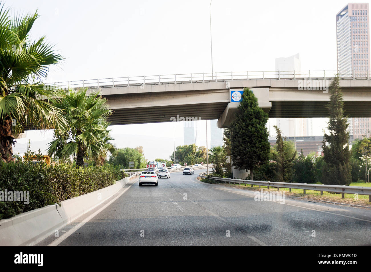 Izmir, Turchia - 8 Agosto 2018: palme e ponte su una strada con Folkart torri e alcuni posti auto sulla strada Altinyola. Foto Stock