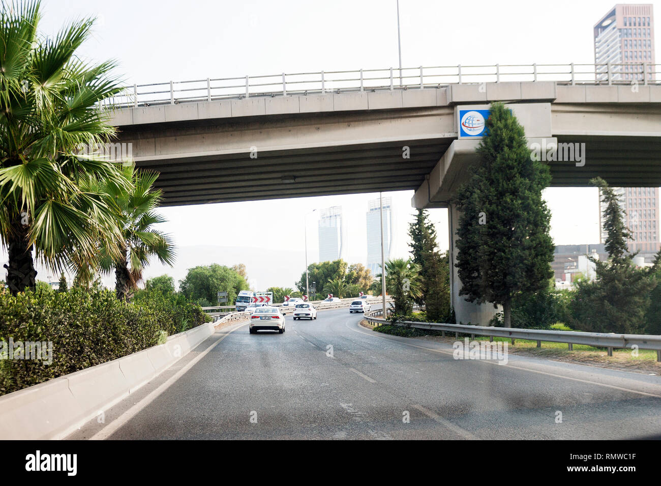 Izmir, Turchia - 8 Agosto 2018: palme e ponte su una strada con Folkart torri e alcuni posti auto sulla strada Altinyola. Foto Stock