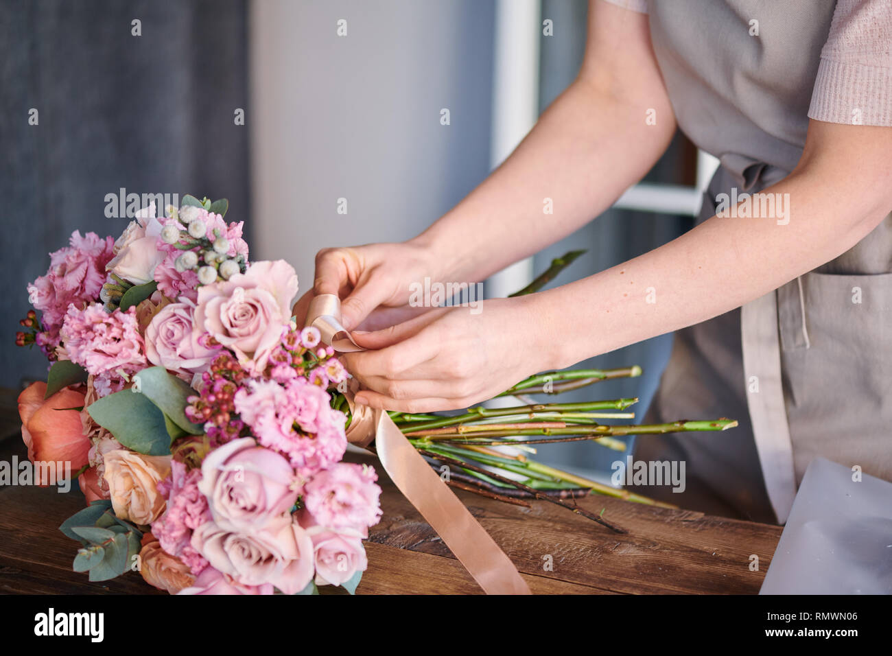 Proprietario del fioraio o studio beige legatura a nastro di seta intorno al mucchio di fresche rose pastello su tavola Foto Stock
