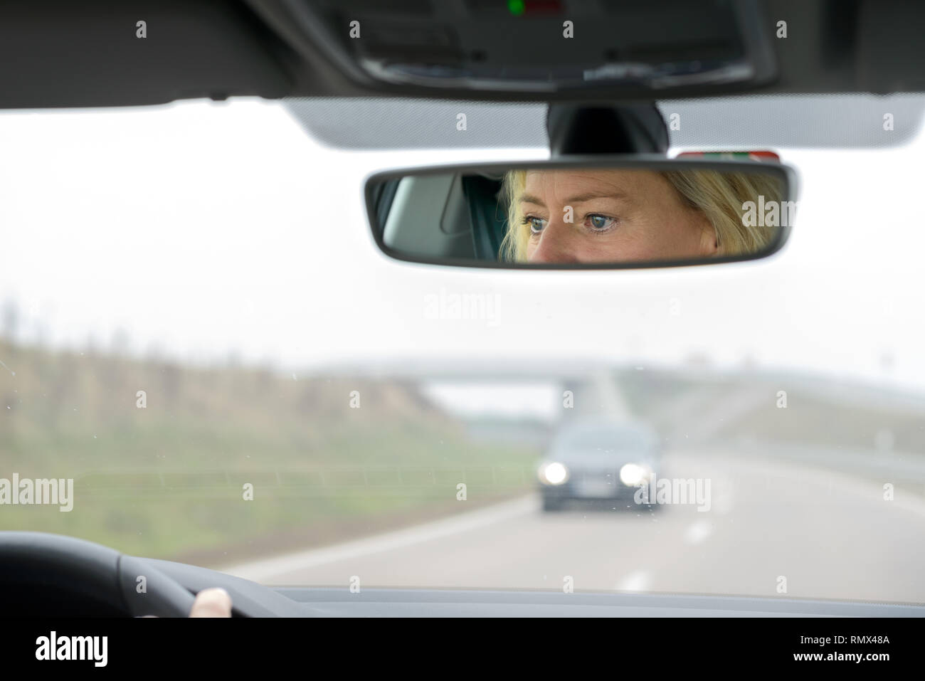 Donna alla guida di una vettura su una autostrada che si avvicinano ad un ponte su un nebbioso giorno con i suoi occhi riflessa nello specchio Foto Stock