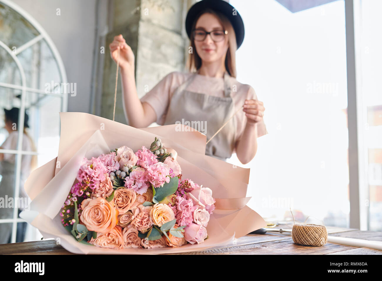Grande mazzo di freschi di rose e altri fiori avvolti in carta giacente sul tavolo mentre un fioraio legatura con filo Foto Stock