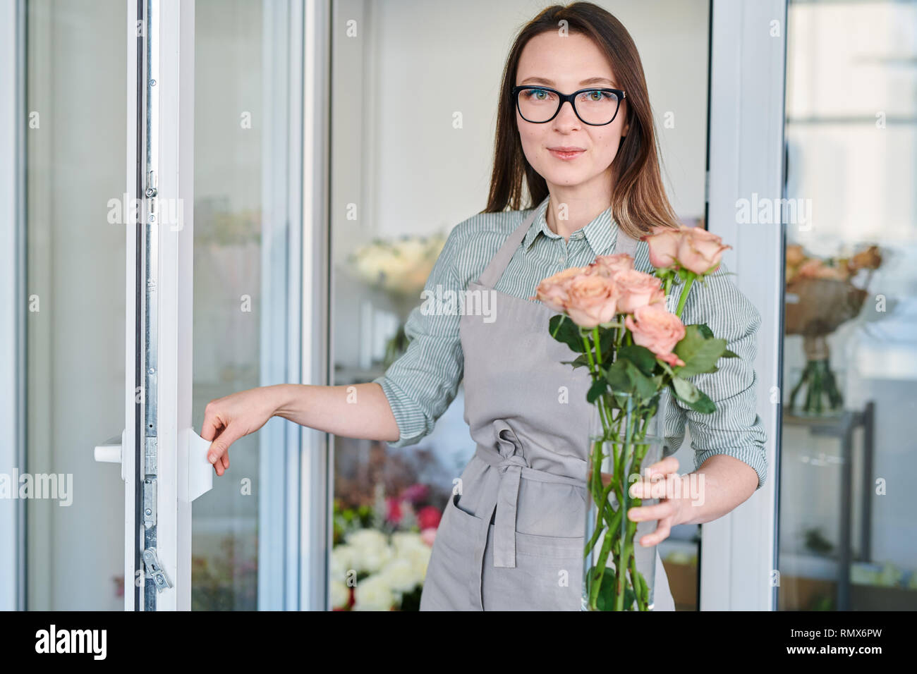 Giovani fioraio di aprire lo sportello del frigorifero mentre porta vaso con mazzo di rose pastello Foto Stock