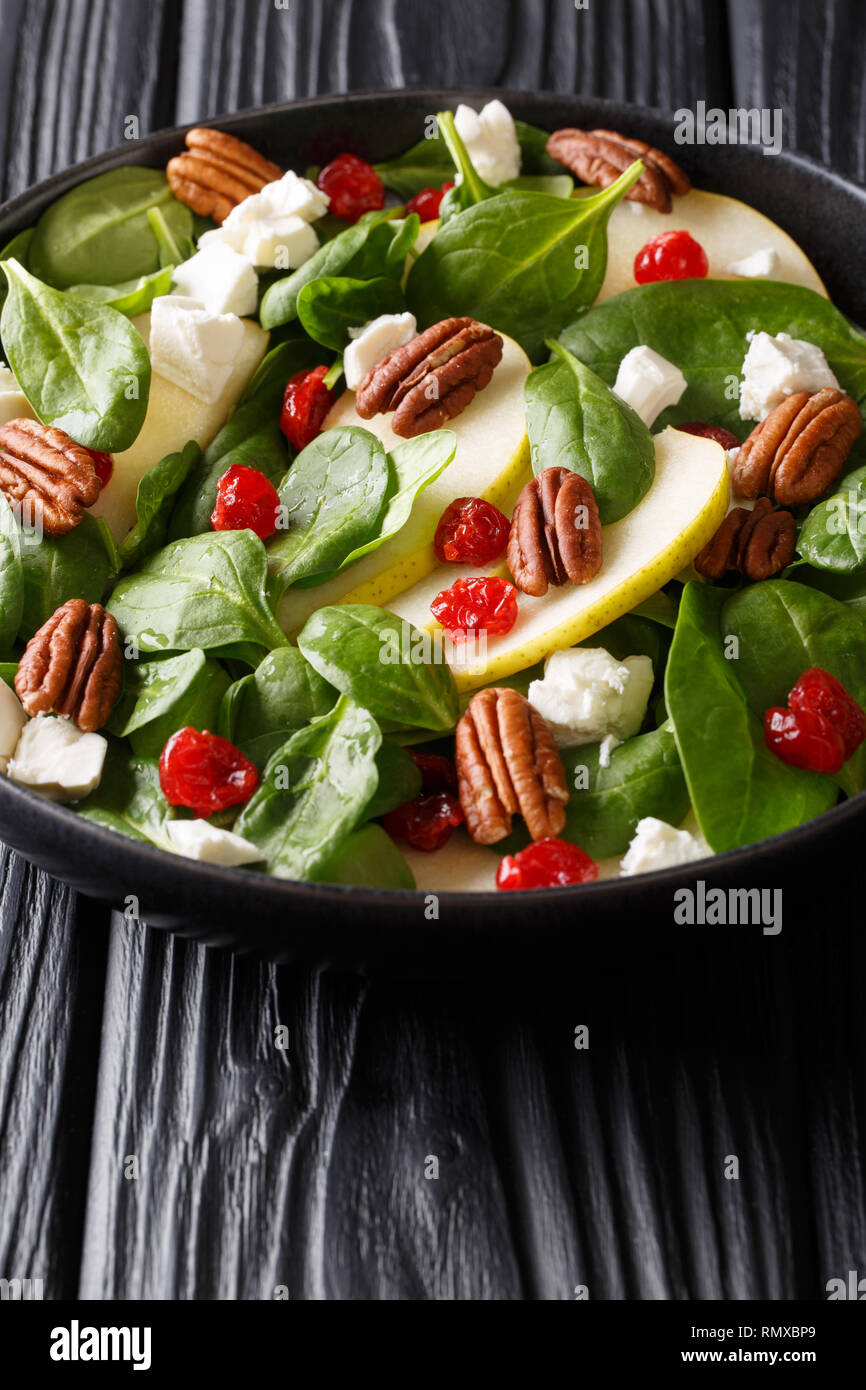 Insalata di naturale con pere fresche, verde di spinaci, le noci pecan, il formaggio feta e le ciliegie secche close-up su una piastra sul piano verticale. Foto Stock