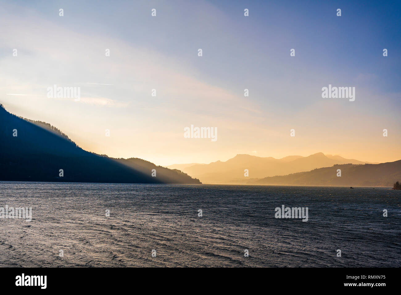 Paesaggio con montagne e colline con foresta illuminata dai raggi obliqui del sole al tramonto sulle rive del fiume Columbia con acqua Foto Stock