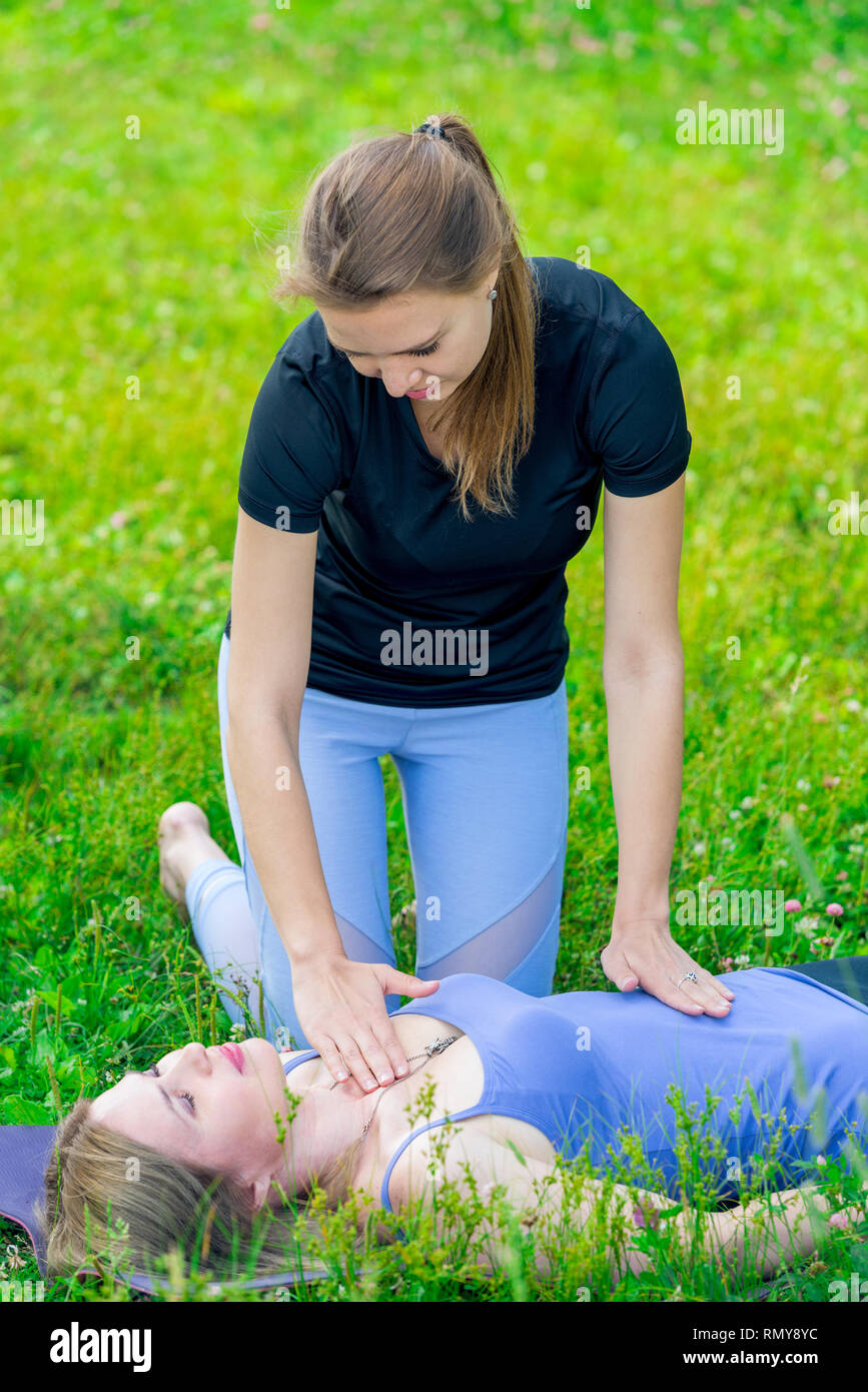 Un allenatore esperto controlla la donna di respirazione durante una lezione di yoga nel parco Foto Stock