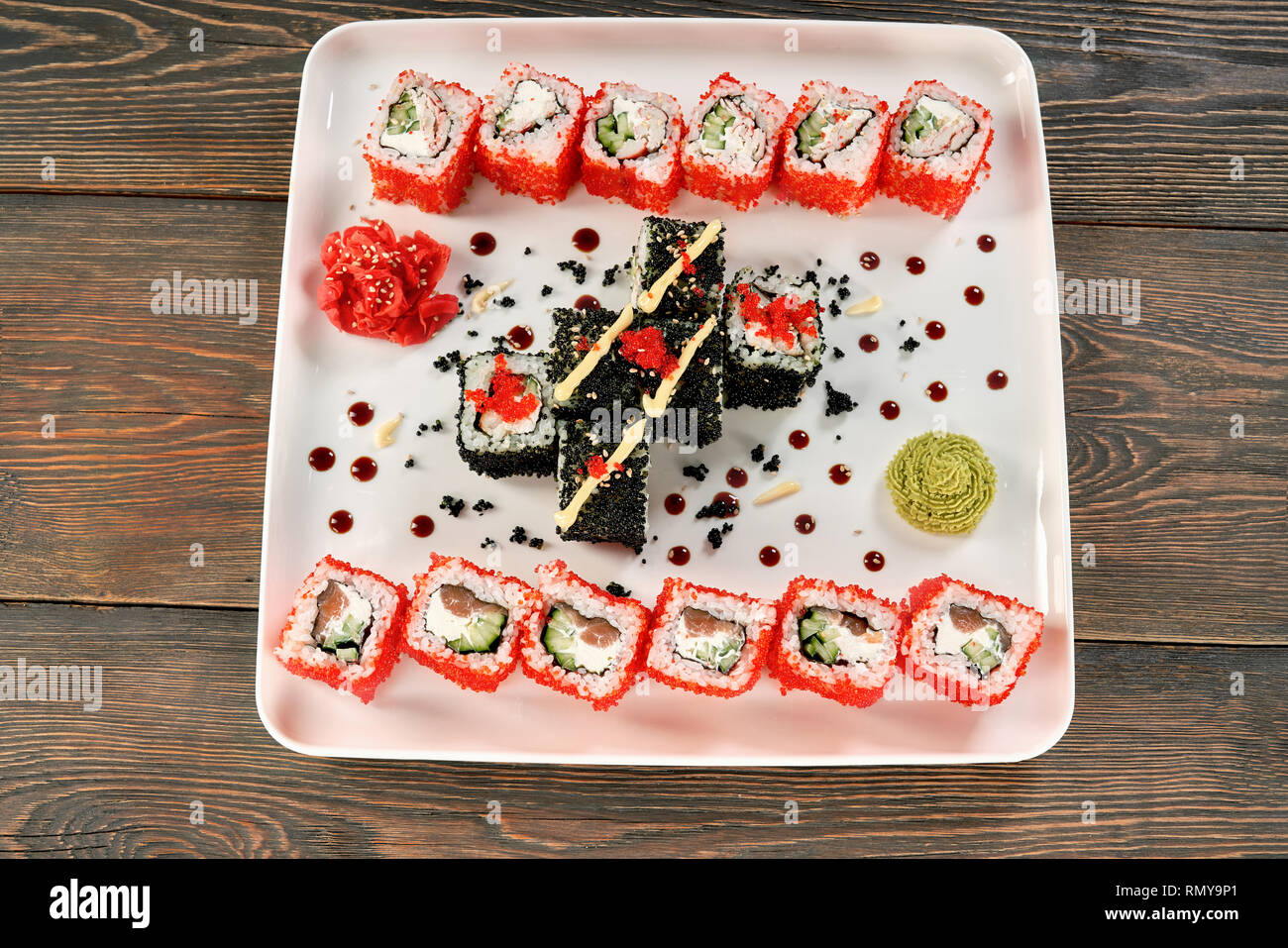 Rotoli di Philadelphia con salmone, crema di formaggio e cetriolo. Uramaki sushi set decorato con mayo, wasabi e zenzero sott'aceto, coperto di rosso tobiko roe, presentato su piastra bianca. Foto Stock