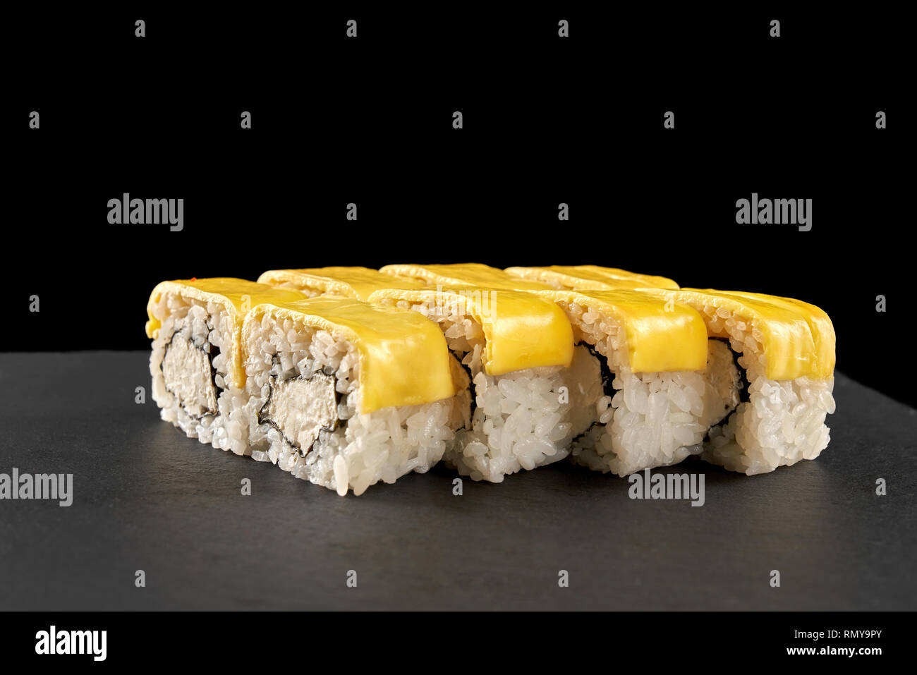 Formaggio uramaki sushi rotoli ricoperti di formaggio. Philadelphia rotoli farciti di crema di formaggio, servita sulla pietra nera piastra. Foto Stock