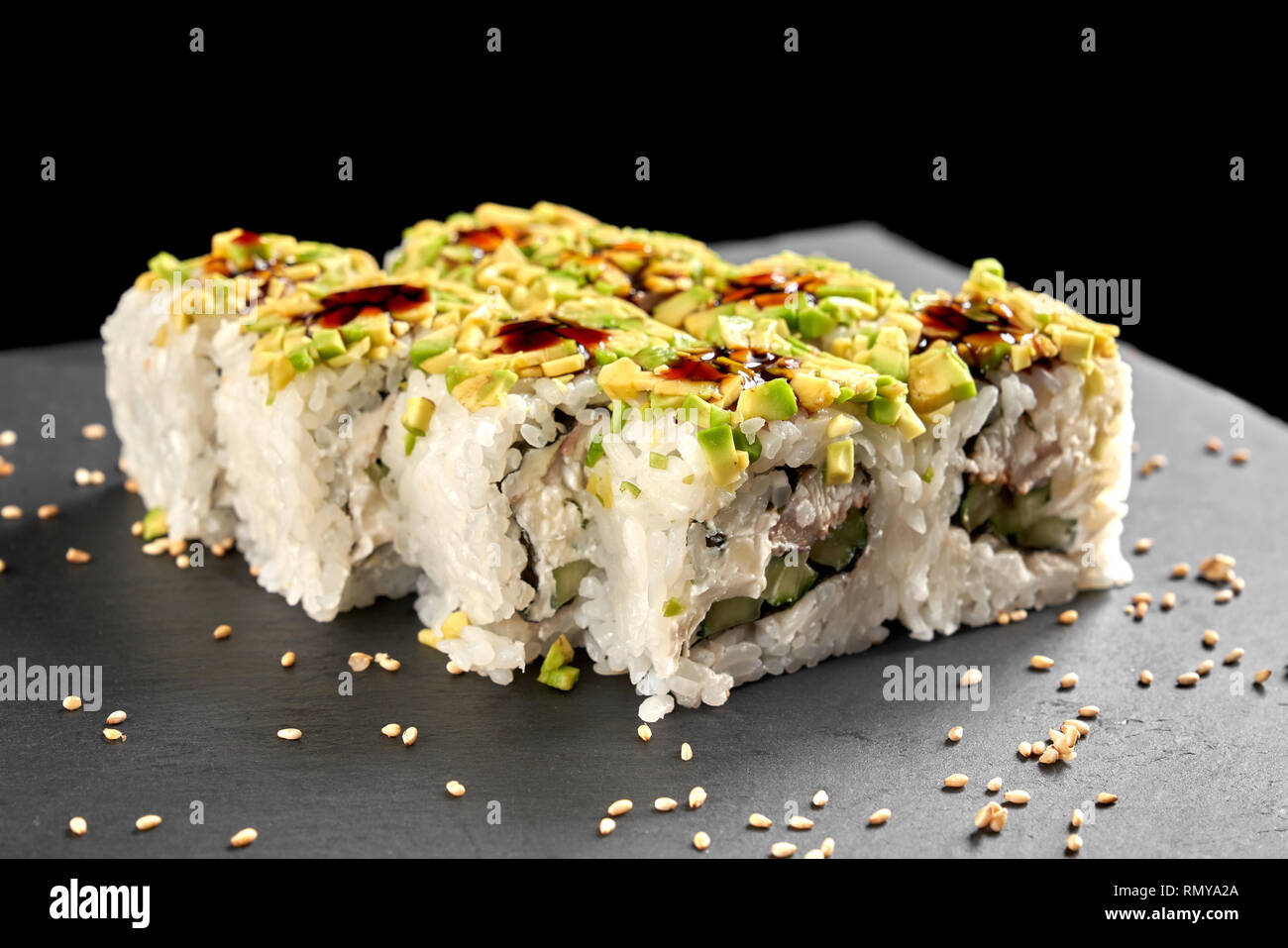 Uramaki rullo rivestito con polpa di avocado e riempito con la crema di formaggio, cetriolo e anguilla affumicata. Sushi condito con salsa di unagi. Foto Stock