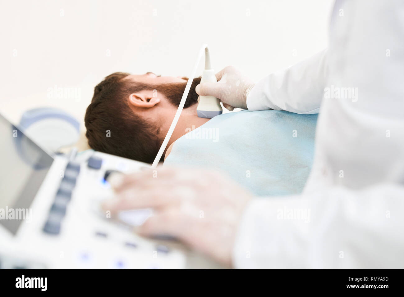 Le mani del medico utilizzando speciali apparecchiature per ultrasuoni ed ecografia diagnostica. Medico indossa in bianco guanti medicali. Paziente di sesso maschile giacente, avente il suo collo ha esaminato, linfonodi. Foto Stock