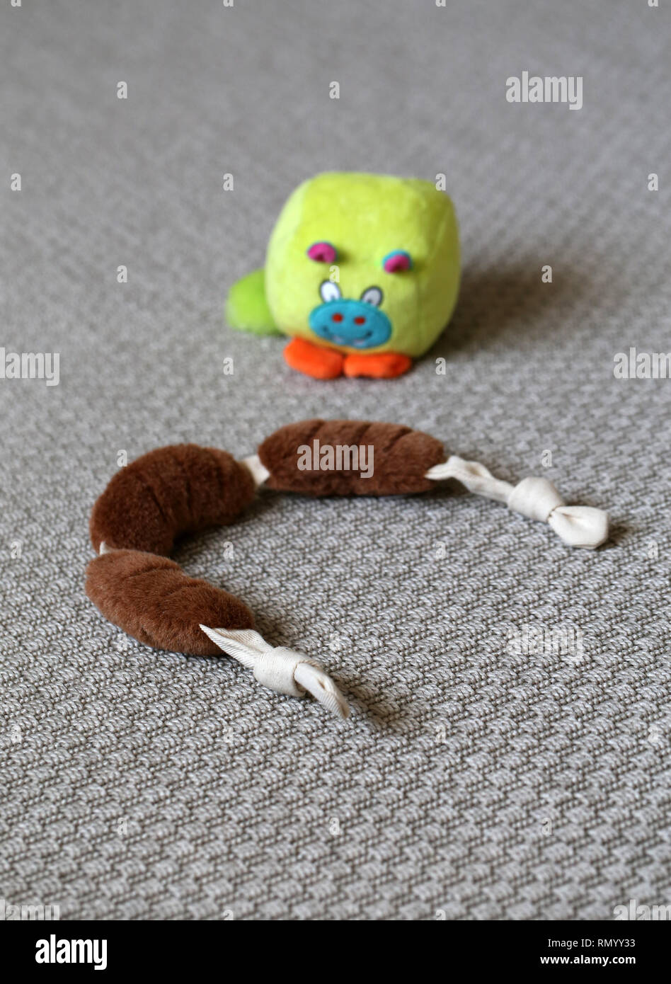 Colorati giocattoli cane su un tappeto grigio. I giocattoli sono marrone ripieni di salsicce e di verde poco monster giocattolo. Carino e giocattoli colorati. Primo piano. Foto Stock