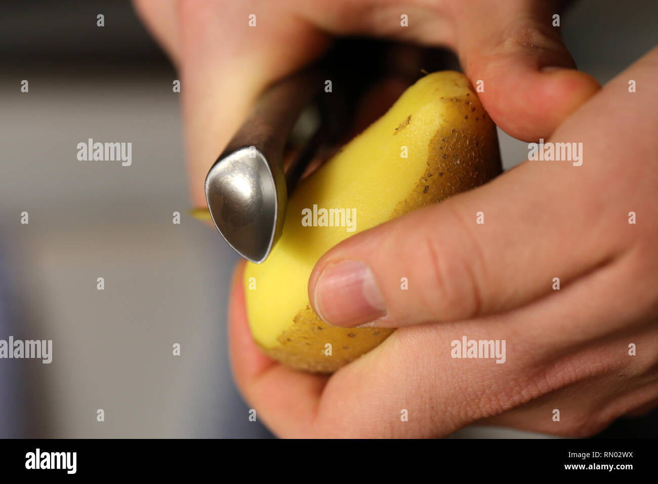 Un uomo pelare patate metallico con un pelapatate. È possibile vedere le mani, una patata e sbucciatore in questa foto. Immagine a colori. Primo piano. Foto Stock