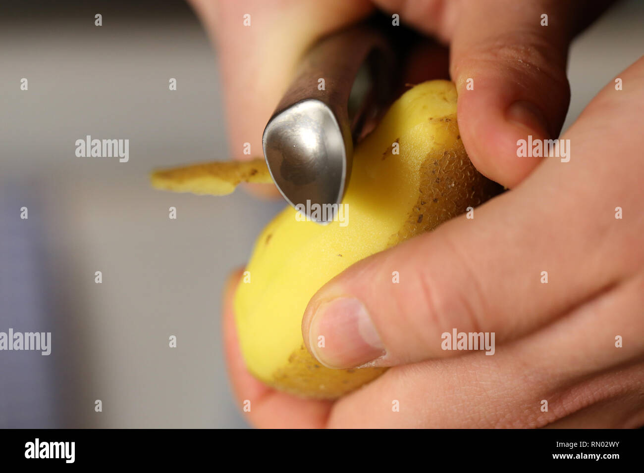 Un uomo pelare patate metallico con un pelapatate. È possibile vedere le mani, una patata e sbucciatore in questa foto. Immagine a colori. Primo piano. Foto Stock