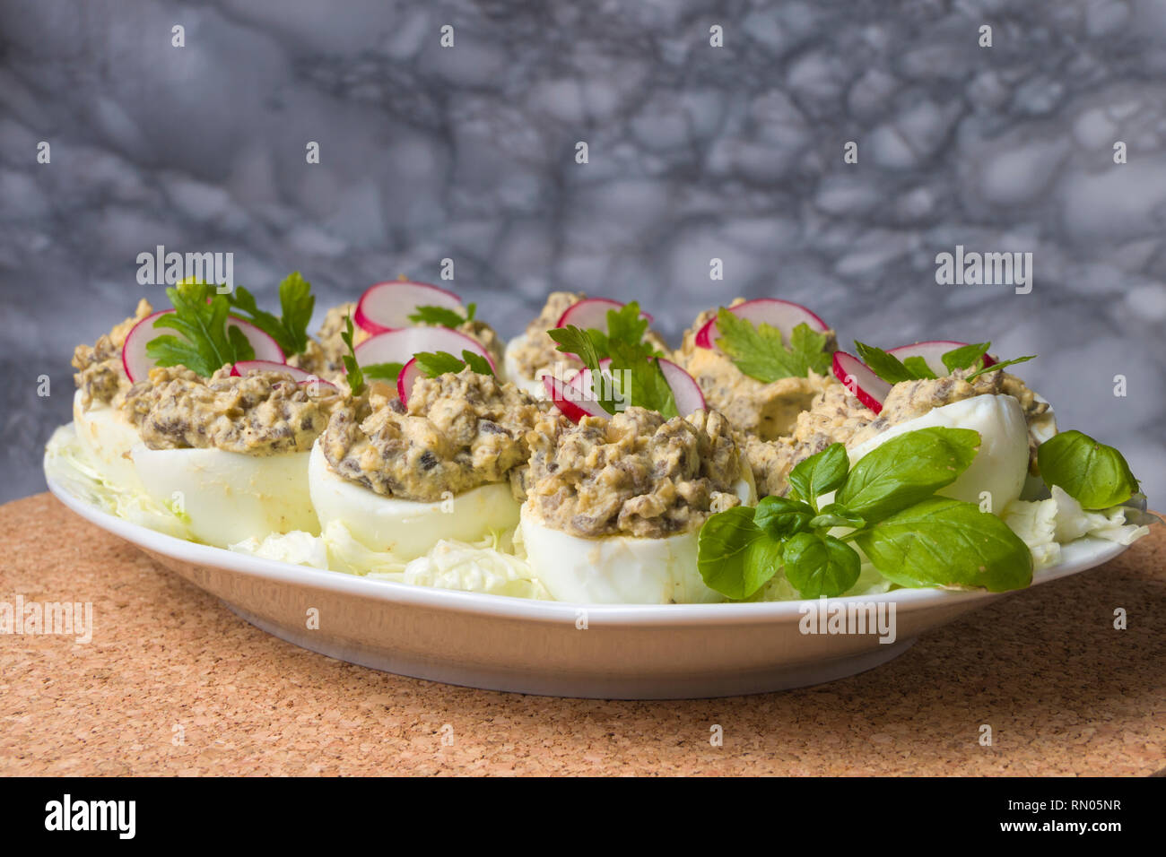 Uova sode farcite con funghi champignon e fette di ravanello, prezzemolo, insalata sulla piastra bianca. Foto Stock