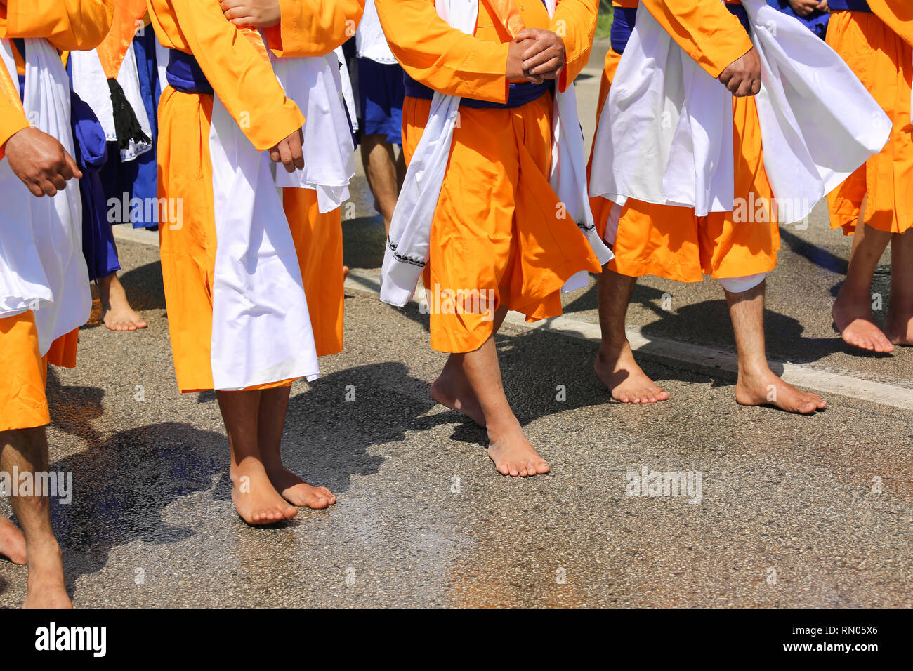 A piedi nudi la religione Sikh uomini durante la sfilata per le strade della città con abiti di colore arancione Foto Stock