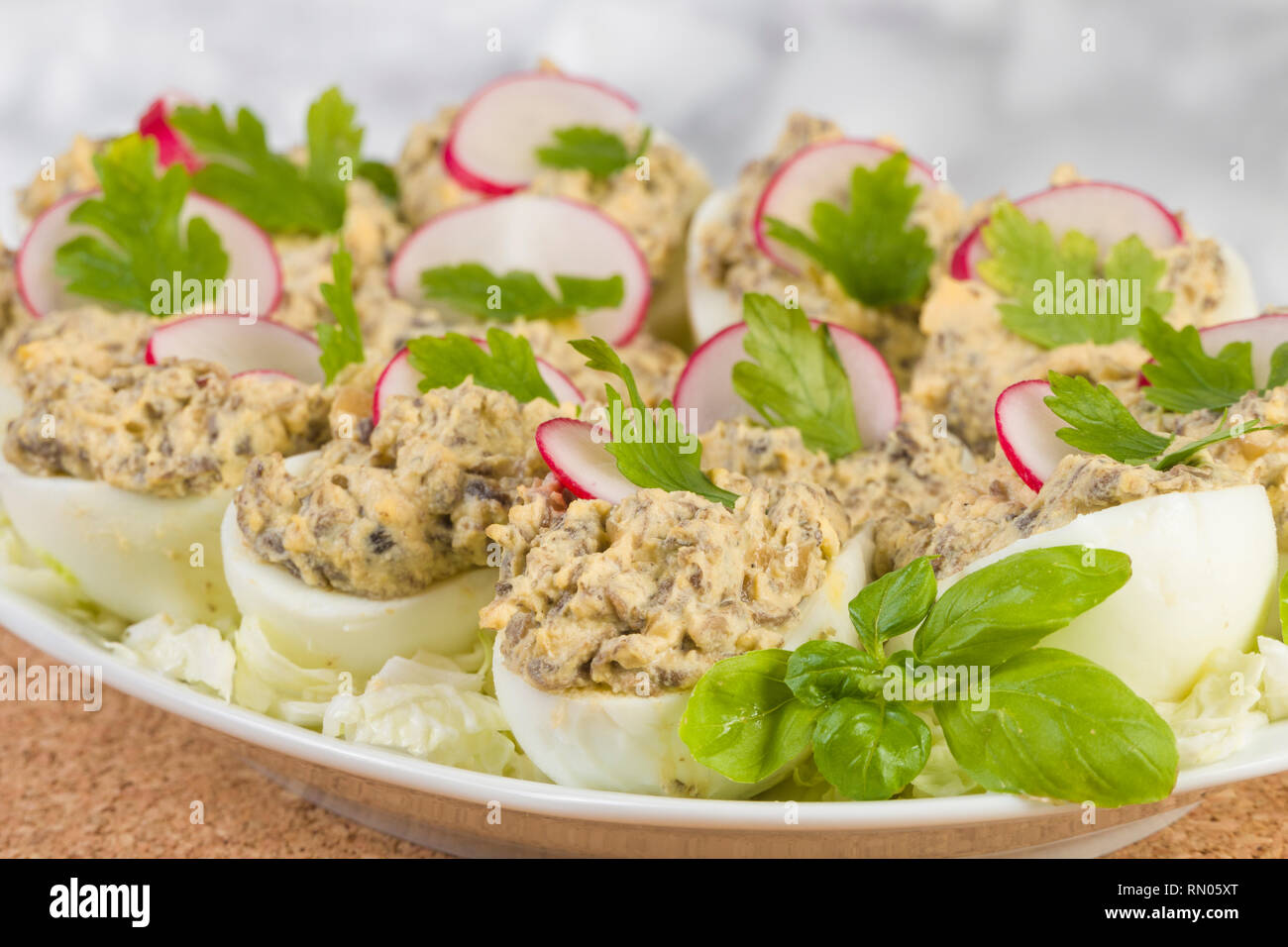 Uova sode farcite con funghi champignon e fette di ravanello, prezzemolo, insalata sulla piastra bianca. Foto Stock