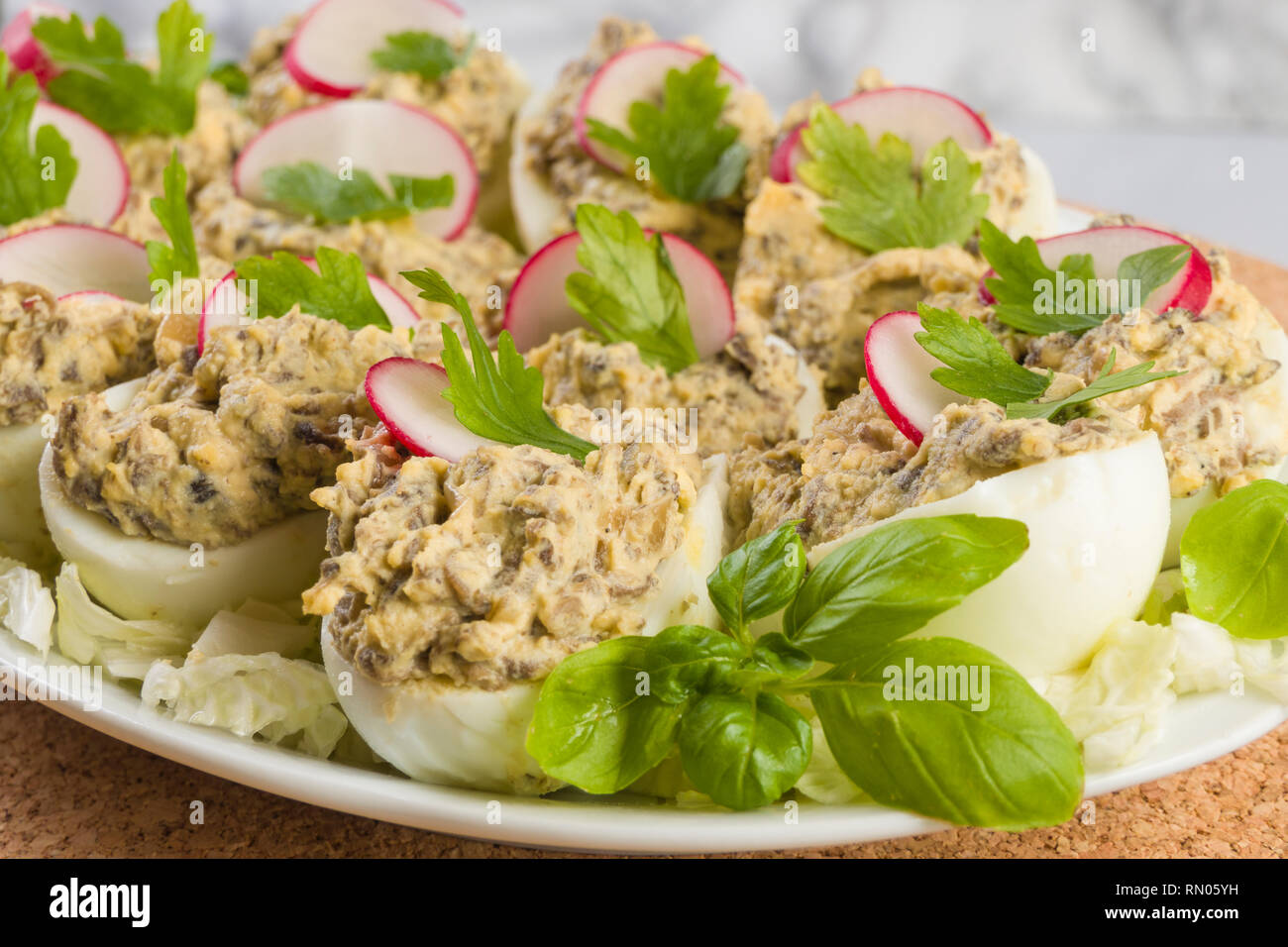 Uova sode farcite con funghi champignon e fette di ravanello, prezzemolo, insalata sulla piastra bianca. Foto Stock