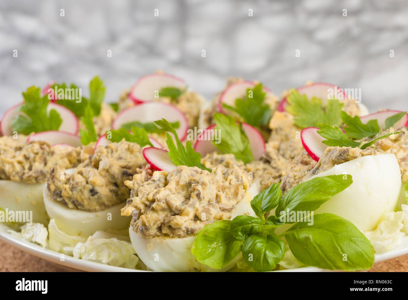 Uova sode farcite con funghi champignon e fette di ravanello, prezzemolo, insalata sulla piastra bianca. Foto Stock