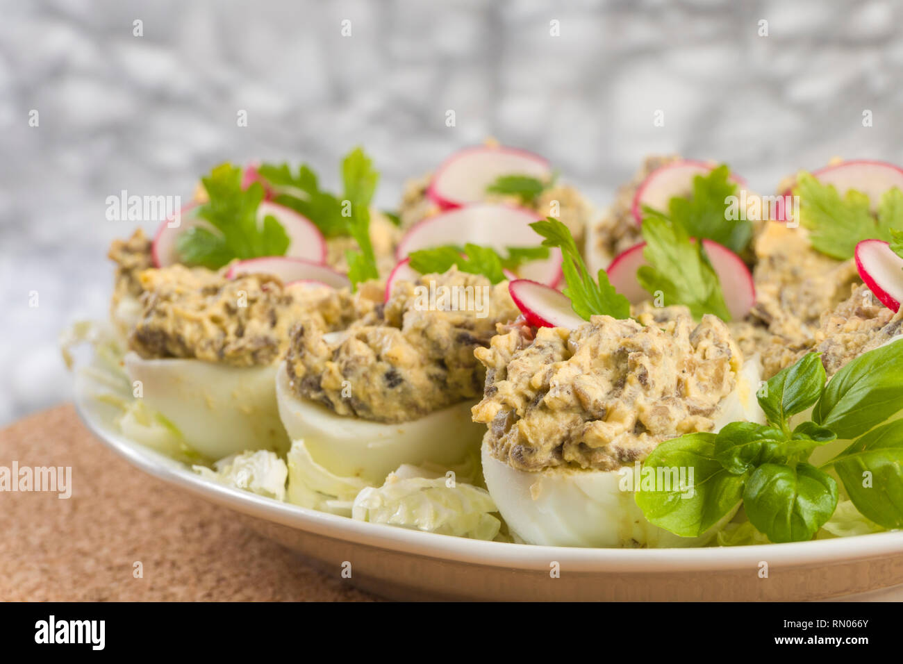 Uova sode farcite con funghi champignon e fette di ravanello, prezzemolo, insalata sulla piastra bianca. Foto Stock