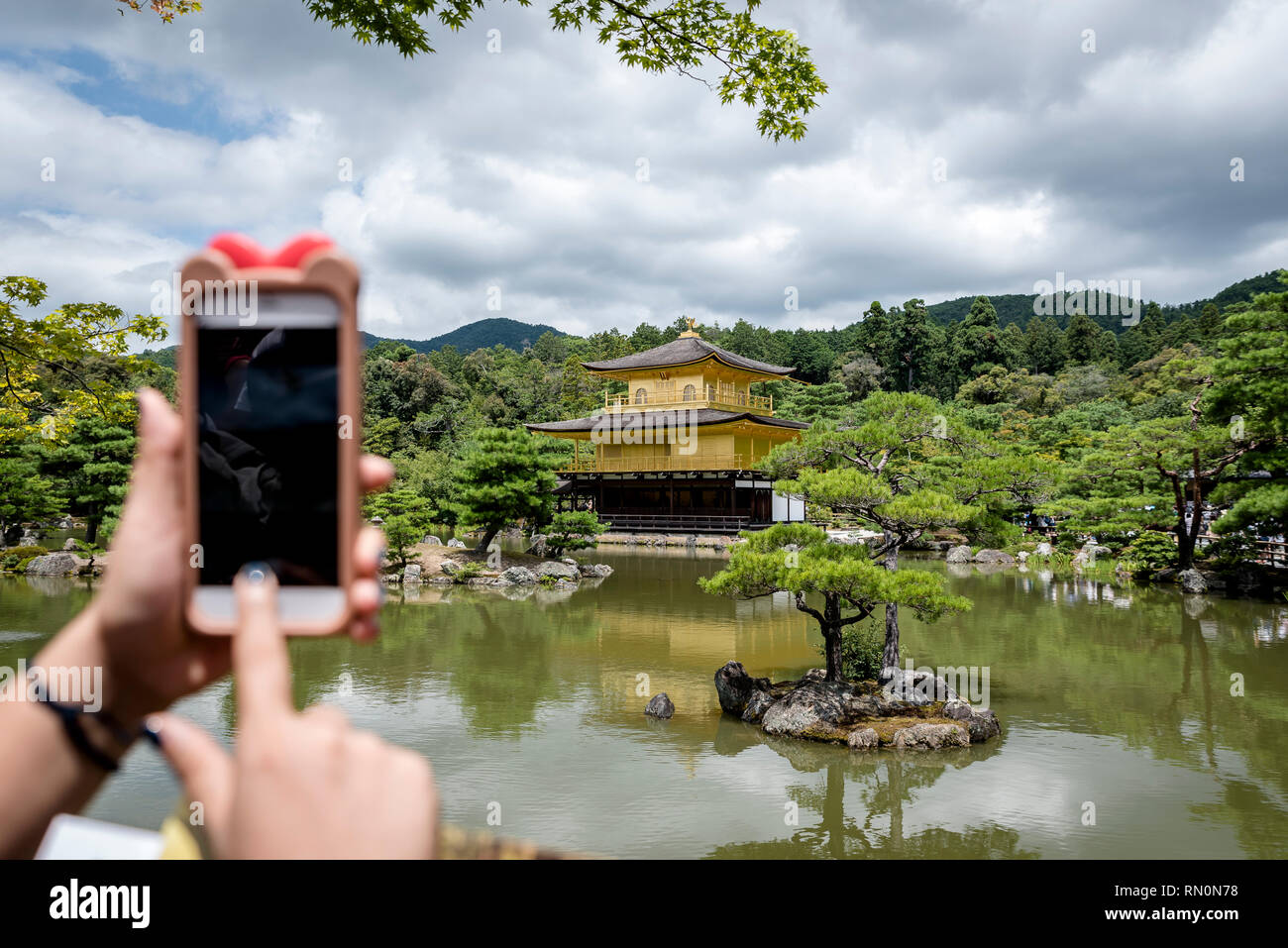 Un turista di scattare una foto del Padiglione Dorato, situato a Kyoto, in Giappone, con uno smartphone. Il tempio è tradizionalmente noto come Kinkaku-ji. Foto Stock