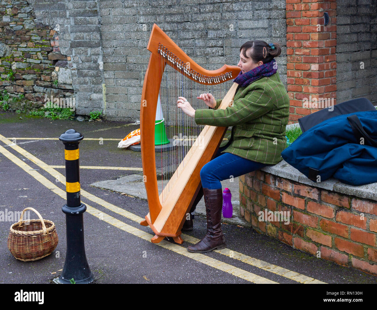 busker femminile che gioca un'arpa per soldi seduti su un muro di mattoni Foto Stock