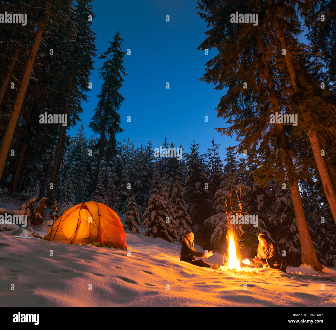 Giovane camping con falò e tenda all'aperto in inverno Foto Stock