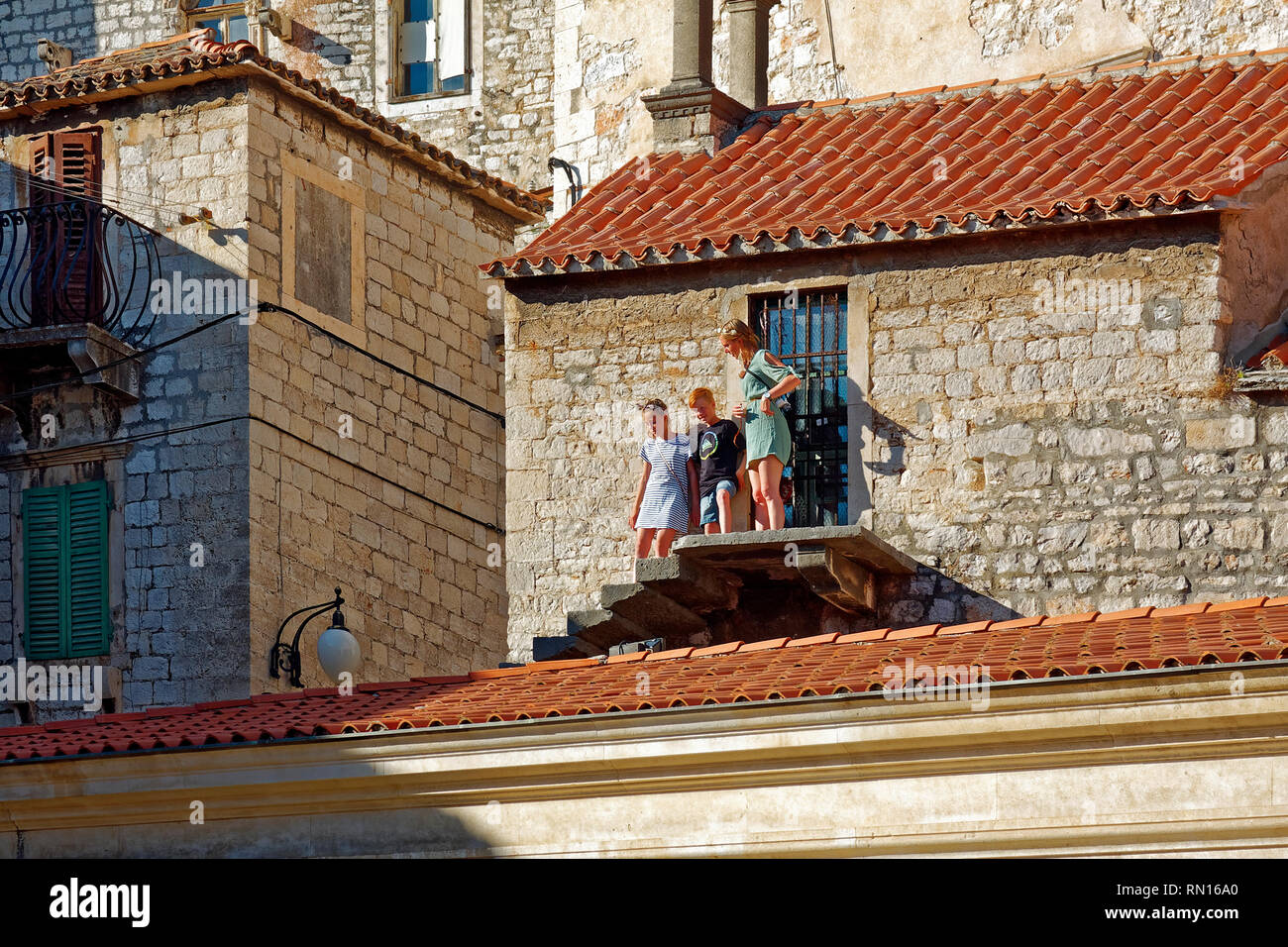 Madre, 2 bambini; fasi sopra rosso tetto di tegole; no ringhiera; abbracciando parete, pericolose; alta; vecchi edifici in pietra; la Piazza della Repubblica; Dalmazia; Sibenik; Cro Foto Stock