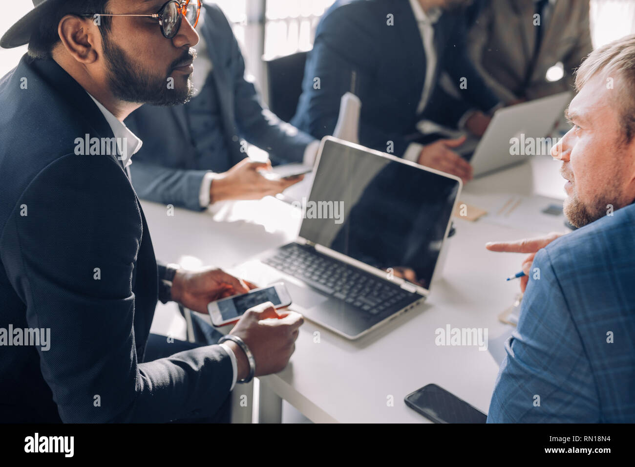 Indiano investitore intelligente, in business suit e hat, cercando seriamente attraverso bicchieri a uomini di affari in ufficio per discutere idee di progetti con partner Foto Stock