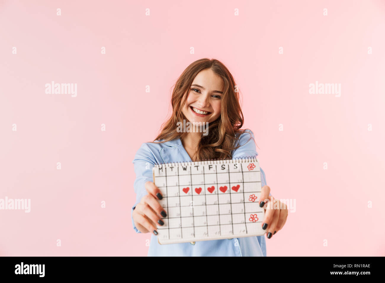 Giovane e bella donna che indossa pigiami in piedi isolato su sfondo rosa, che mostra CALENDARIO MESTRUALE Foto Stock