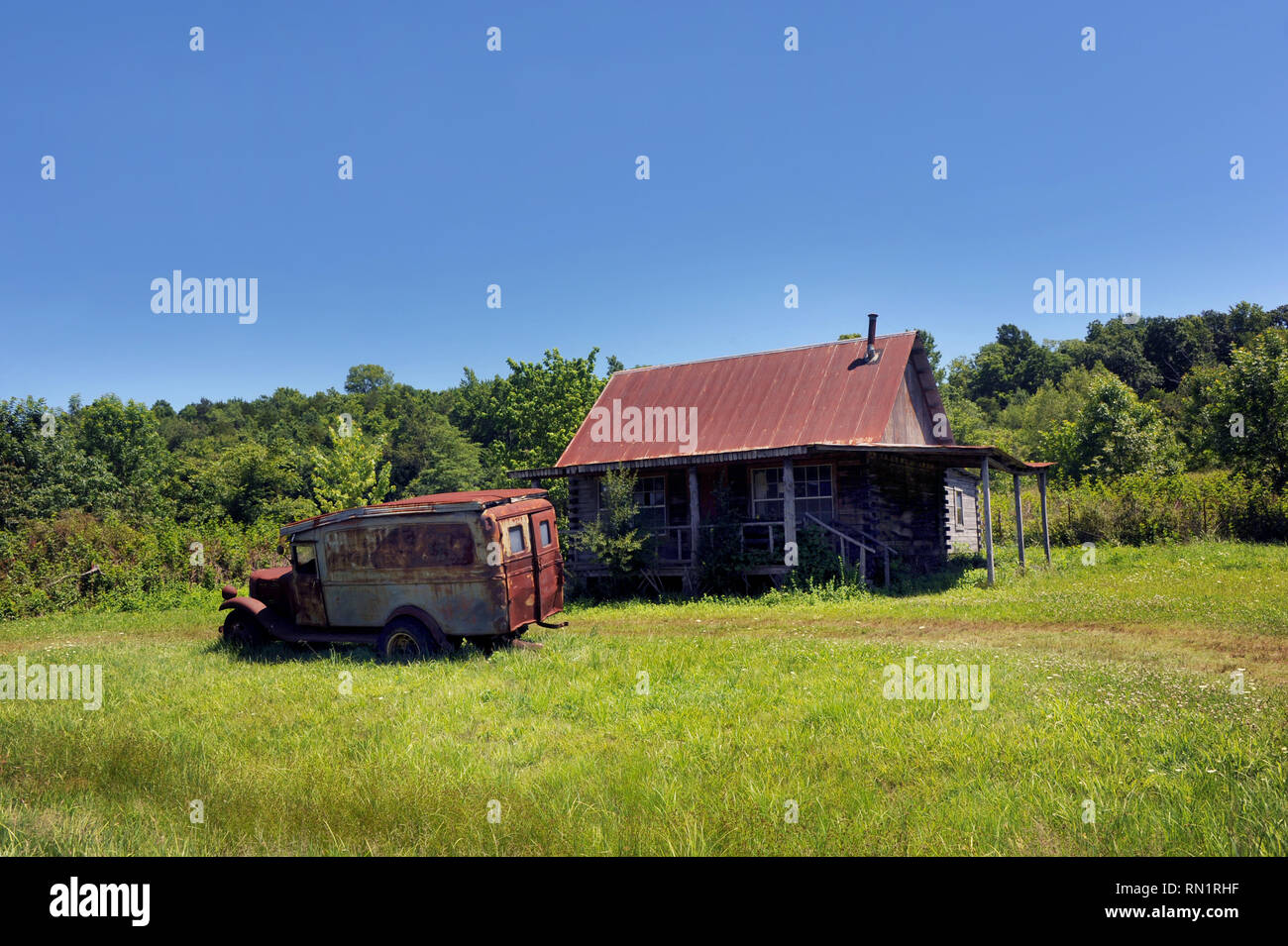 Vecchio jalopy siede nel cantiere di abbandono dei log cabin in Ozark Montagne dell'Arkansas. Cabina è dotata di tetto dello stagno e vecchio carrello è sbiadito cartello hillbilly. Foto Stock