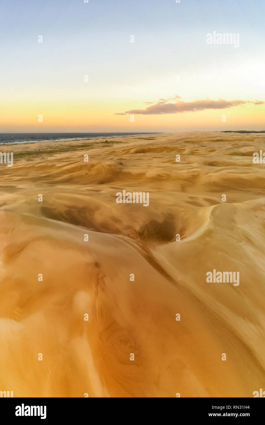 La superficie del terreno per lontano orizzonte e cielo nelle dune di sabbia di Stockton Beach in Australia. Antenna panorama verticale all'alba con una calda luce morbida su sa Foto Stock
