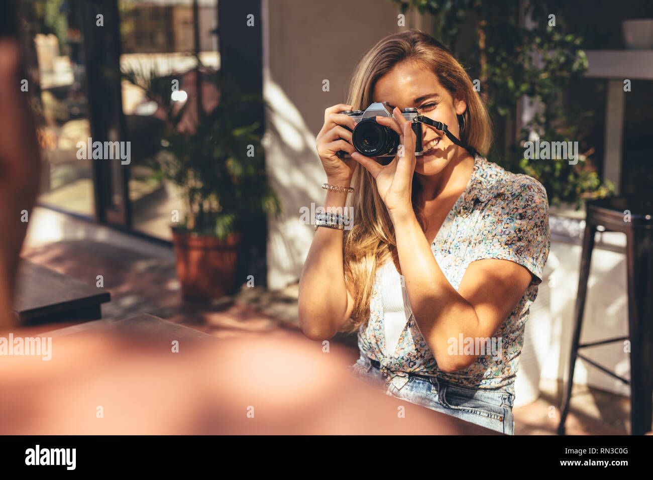 Donna di fotografare i suoi amici con la fotocamera digitale mentre è seduto presso il cafe. L'uomo ottenendo la sua foto selezionato da una femmina di amico per questo social medi Foto Stock