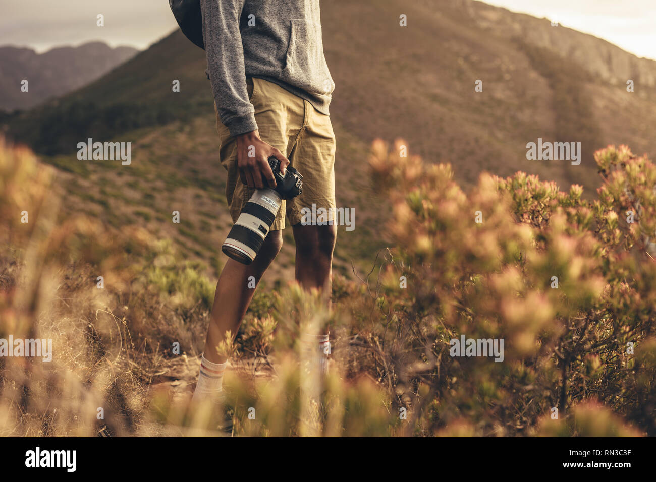 La sezione centrale colpo di uomo in piedi sul sentiero di montagna con la sua fotocamera reflex digitale. Fotografo escursionismo in natura per i nuovi contenuti per il suo social media. Foto Stock