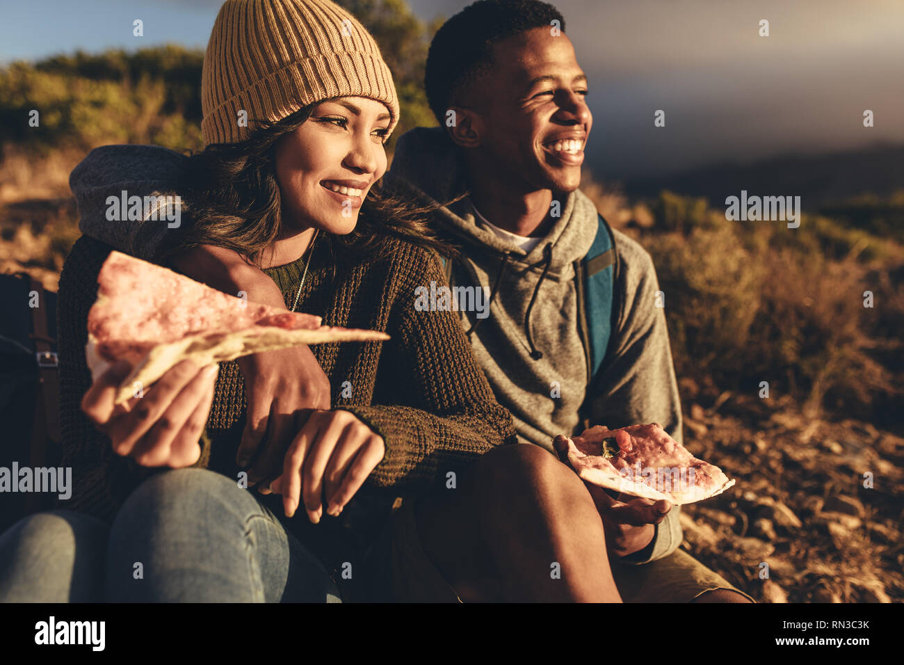 Giovane uomo e donna seduta sul sentiero di montagna di mangiare la pizza e guardando la vista. Coppia in viaggio escursionistico di mangiare la pizza e ammirando la vista. Foto Stock