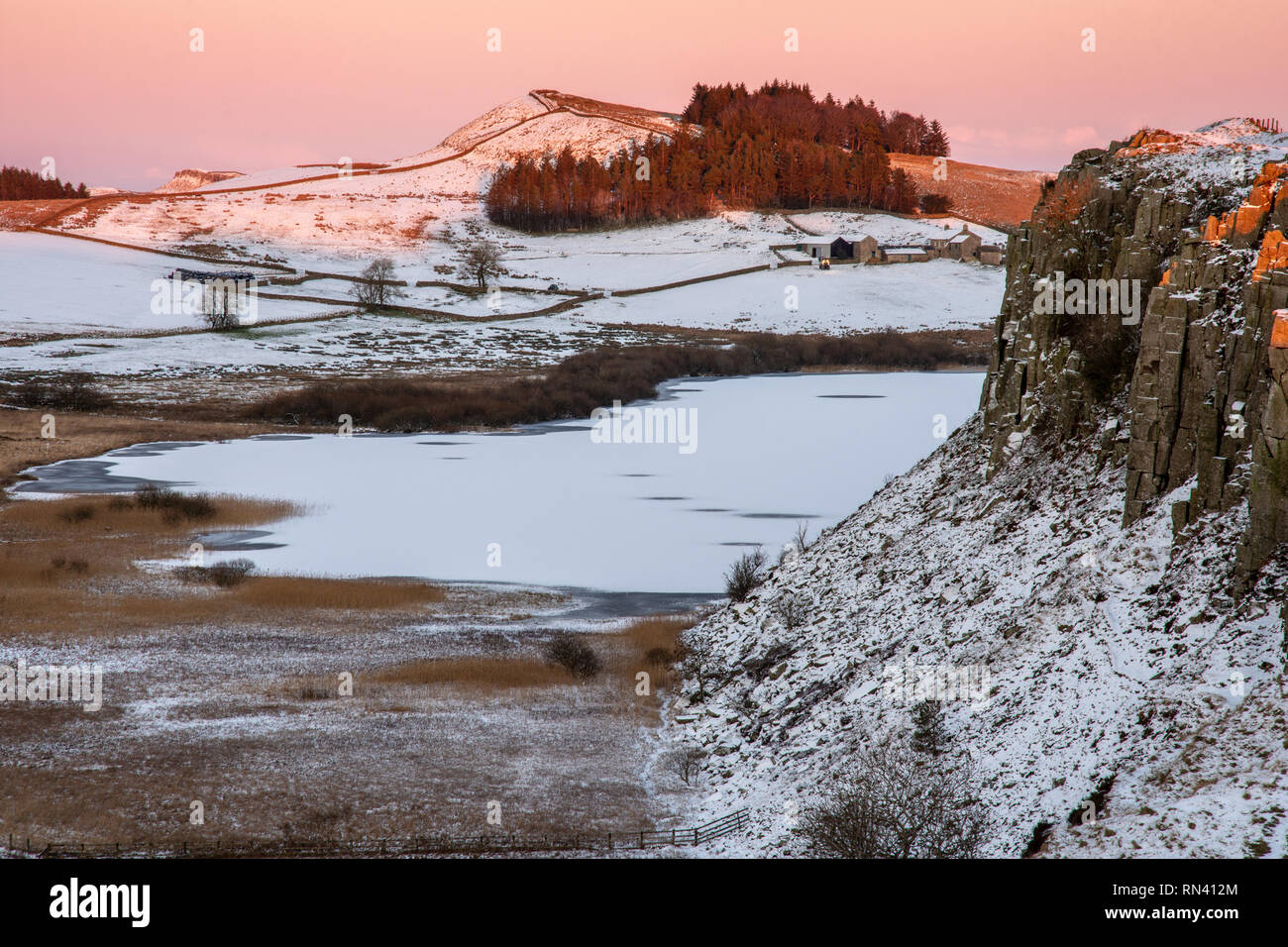 In inverno la neve si trova su campi e dirupi accanto al lago ghiacciato della falesia di Lough il vallo di Adriano in Northumberland. Foto Stock