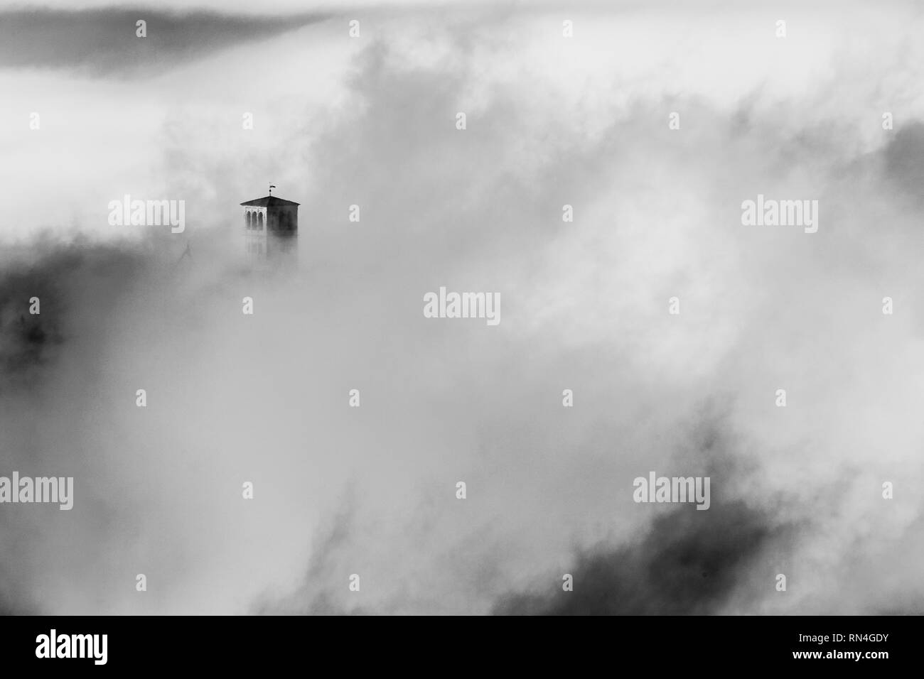 Una vista della Basilica di San Francesco in Assisi (Umbria, Italia) è appena visibile nel mezzo di nebbia Foto Stock