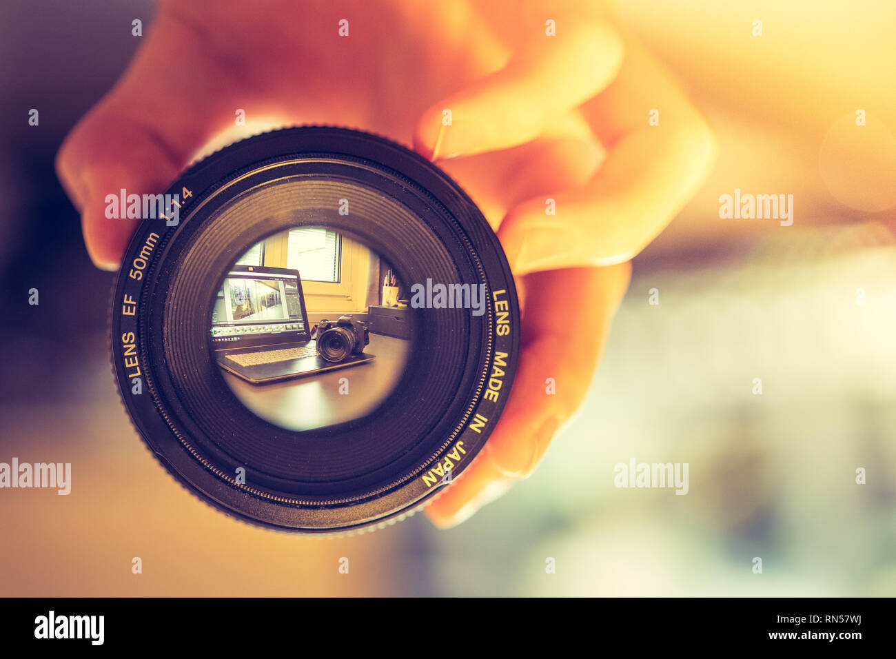 Fotografo detiene una foto professionali ottica in mano. Laptop in uno sfondo sfocato. Foto Stock