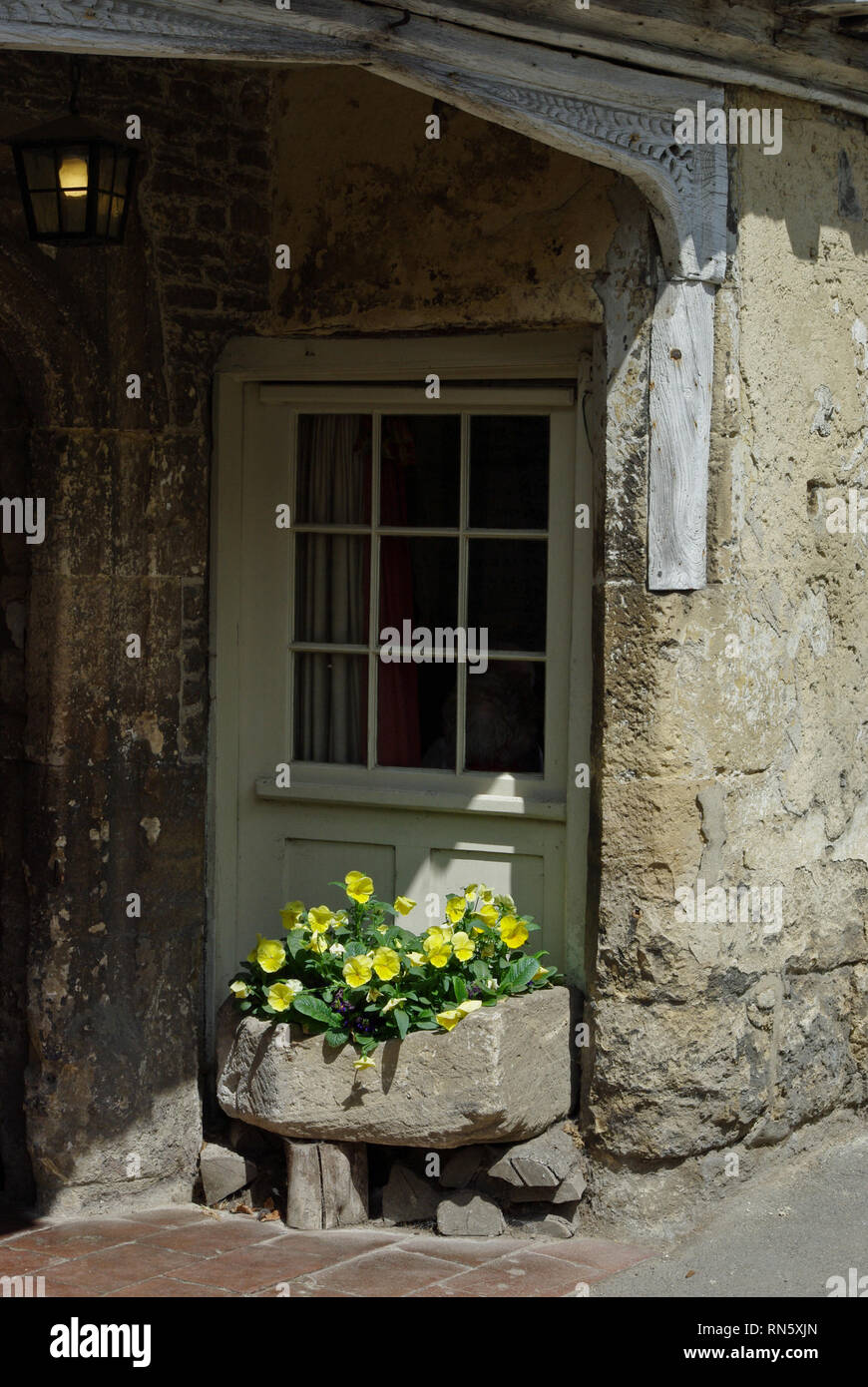 Porta a una vecchia pietra costruito casa con una piantatrice di pietra riempita con fiori di primavera nello storico villaggio di Lacock, Wiltshire, Regno Unito Foto Stock