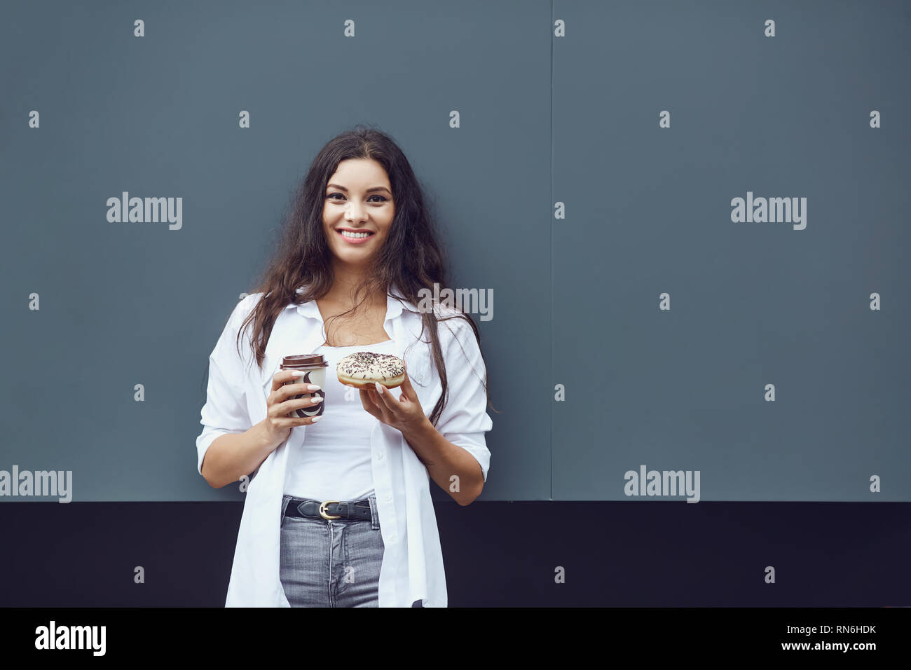 Una bruna ragazza con una tazza da caffè sorride all'aperto. Foto Stock