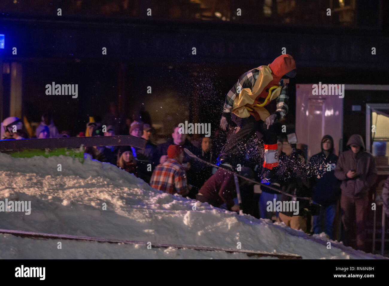 Snowboarder vestito come un hot dog andando fuori una rotaia Foto Stock