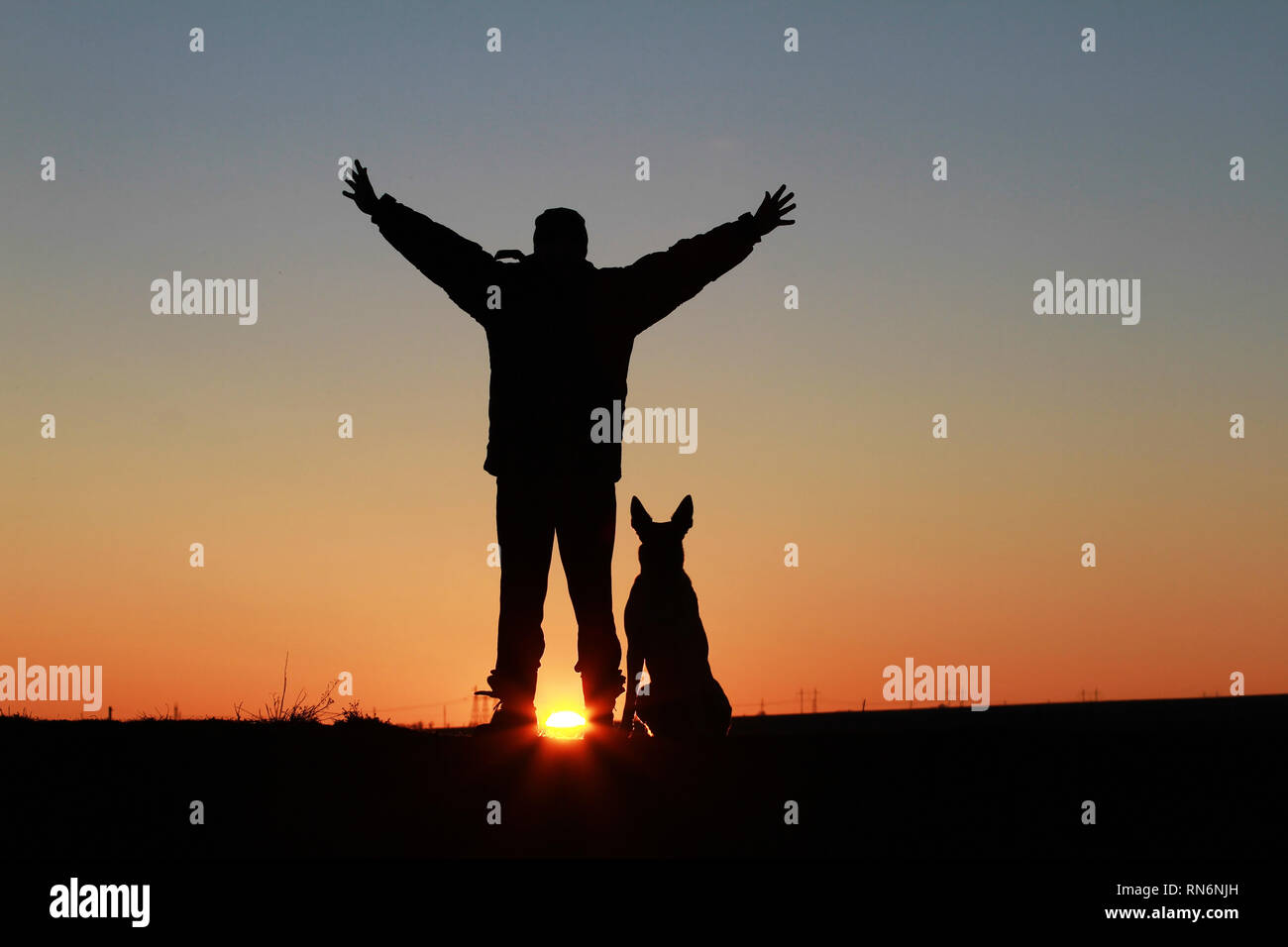 Un uomo e un cane contro lo sfondo di un incredibile tramonto Foto Stock