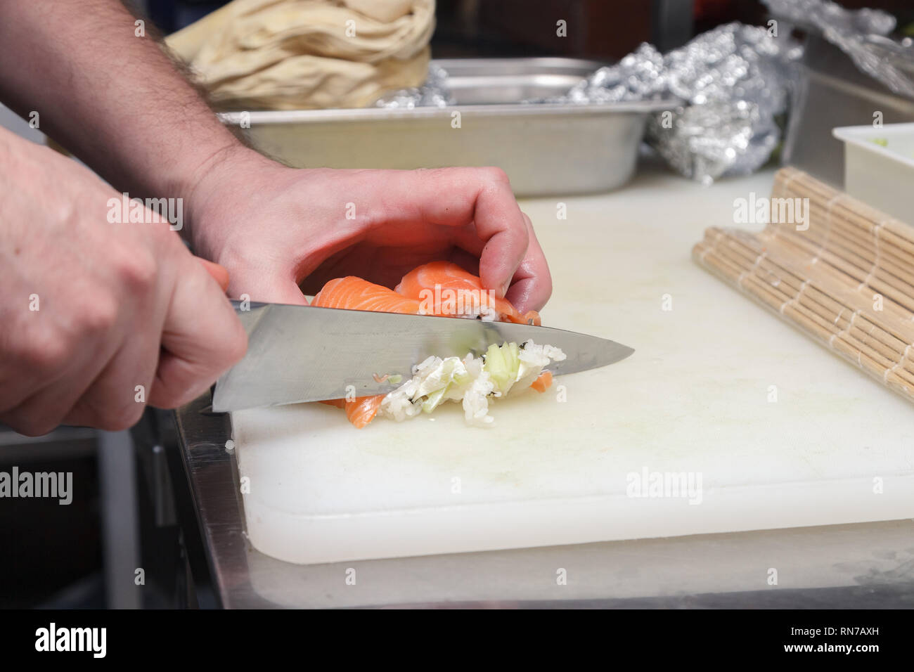 Primo piano della mano è il cuoco che taglia un rotolo di Philadelphia in un ristorante di cucina con un coltello affilato di sushi. Concetto di cucina piatti Giapponesi Foto Stock