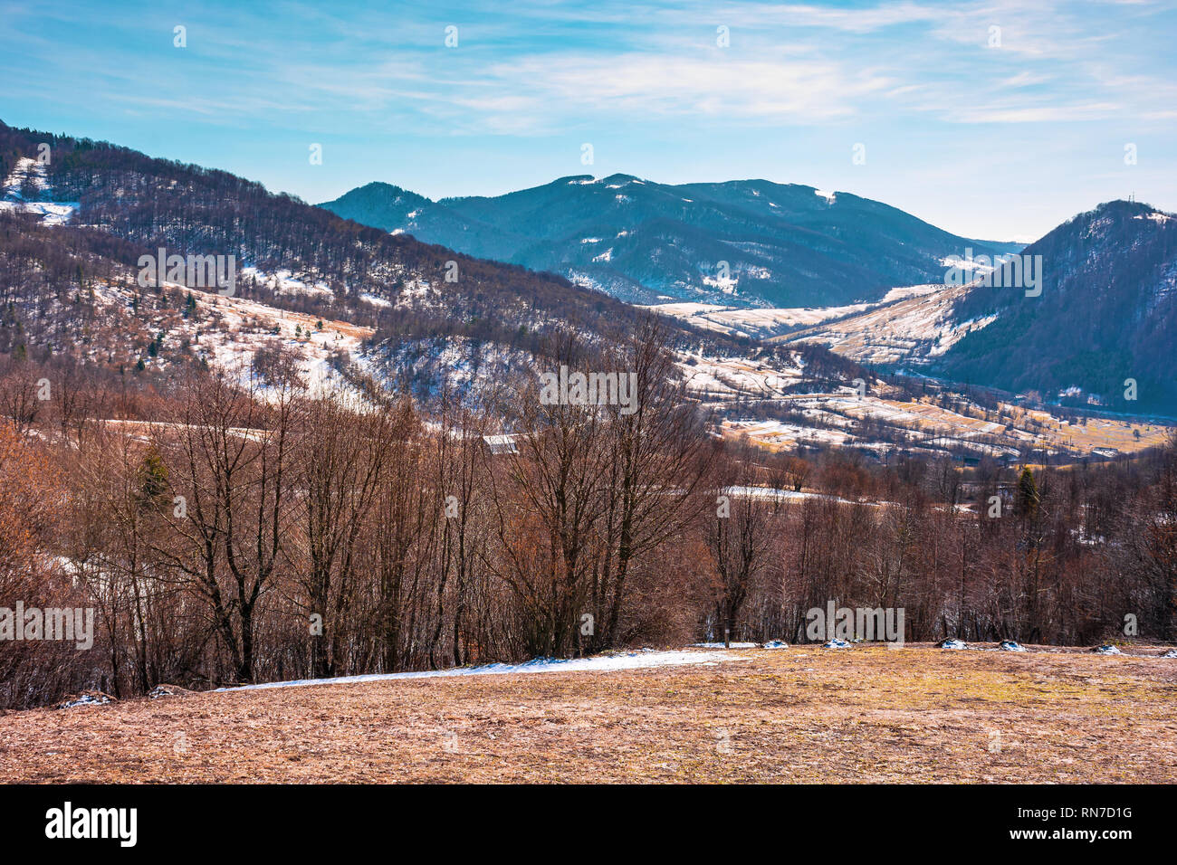 Inizio primavera in campagna montuosa. villaggio nella valle. alberi sfrondato sul prato con erba spiovente e le macchie di neve. La primavera è com Foto Stock