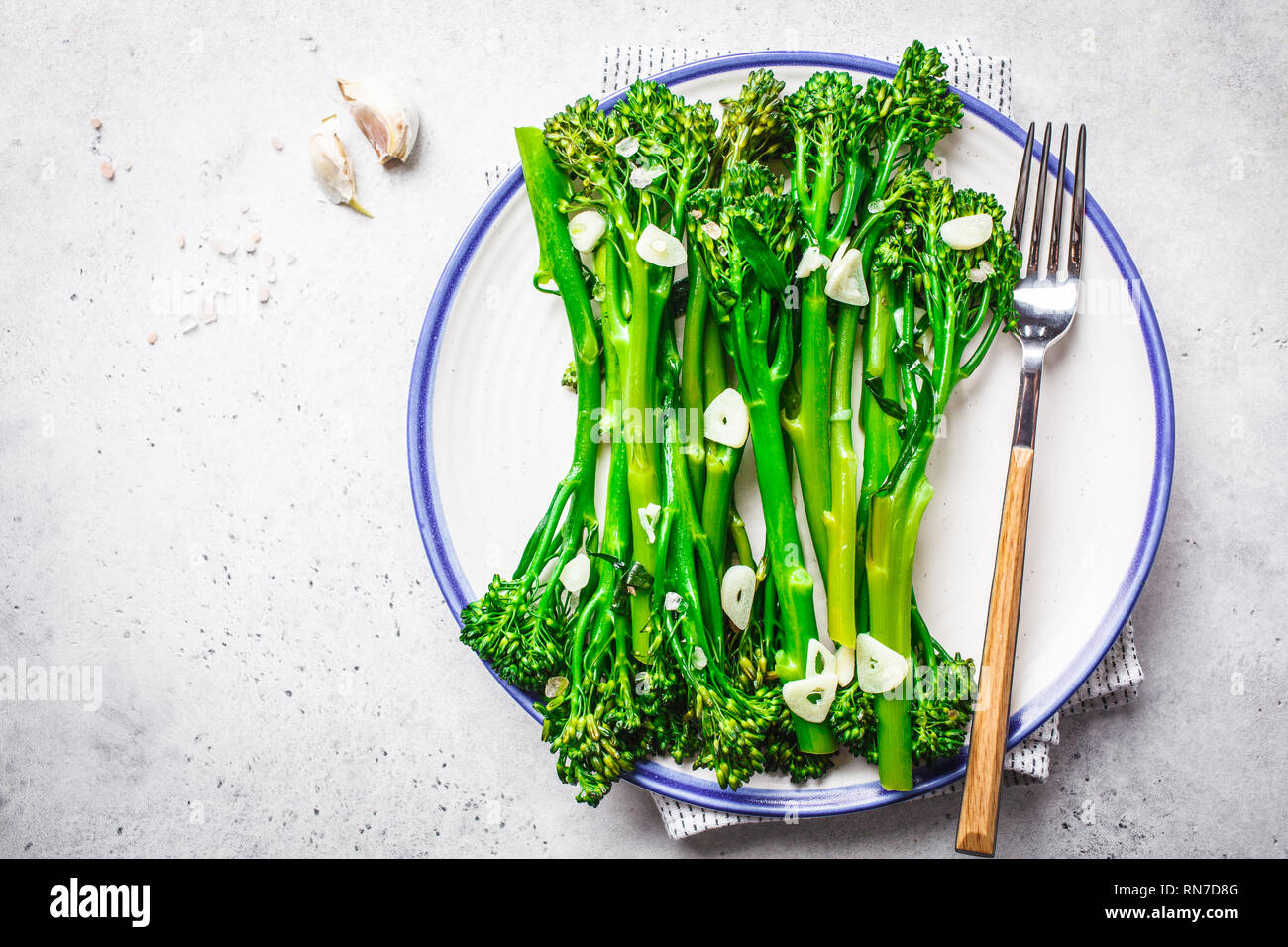 Broccolini bollito con aglio su una piastra bianca. Impianto basato il concetto di cibo. Foto Stock
