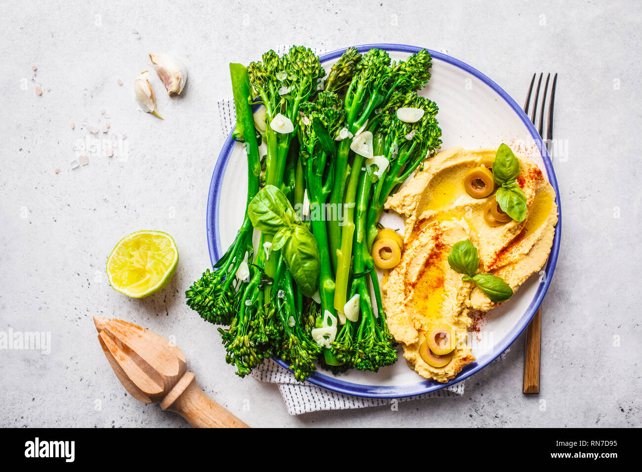 Broccolini cotti con hummus su una piastra bianca, vista dall'alto. Sano cibo vegan concetto. Foto Stock